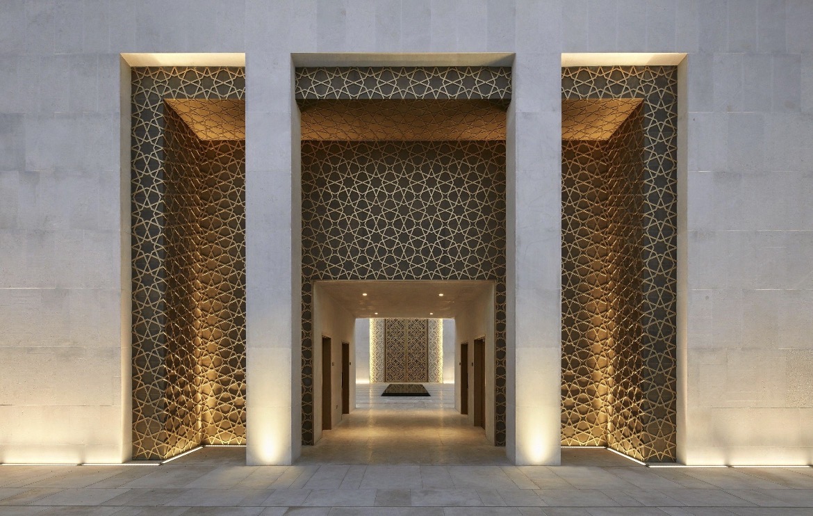 Three illuminated geometric-patterned portals in a modern stone mosque facade